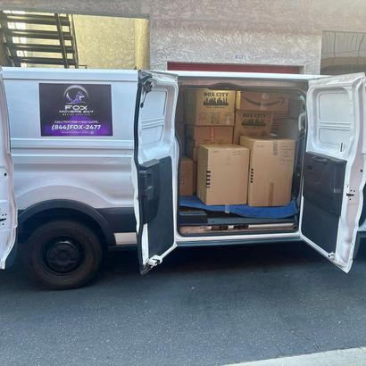 White delivery van with open rear doors, showing stacked cardboard boxes inside.
