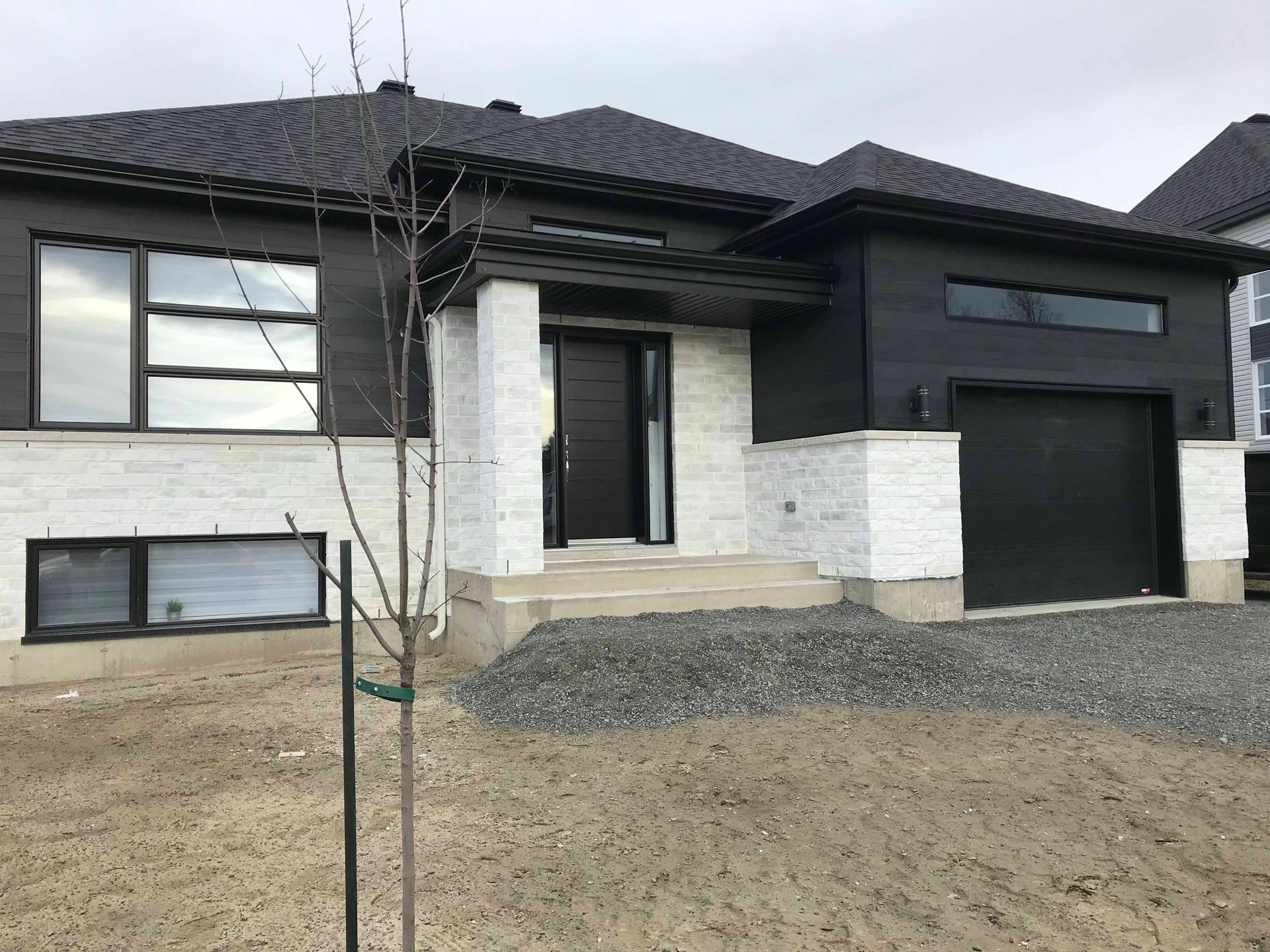 Une maison noire et blanche avec un arbre devant.