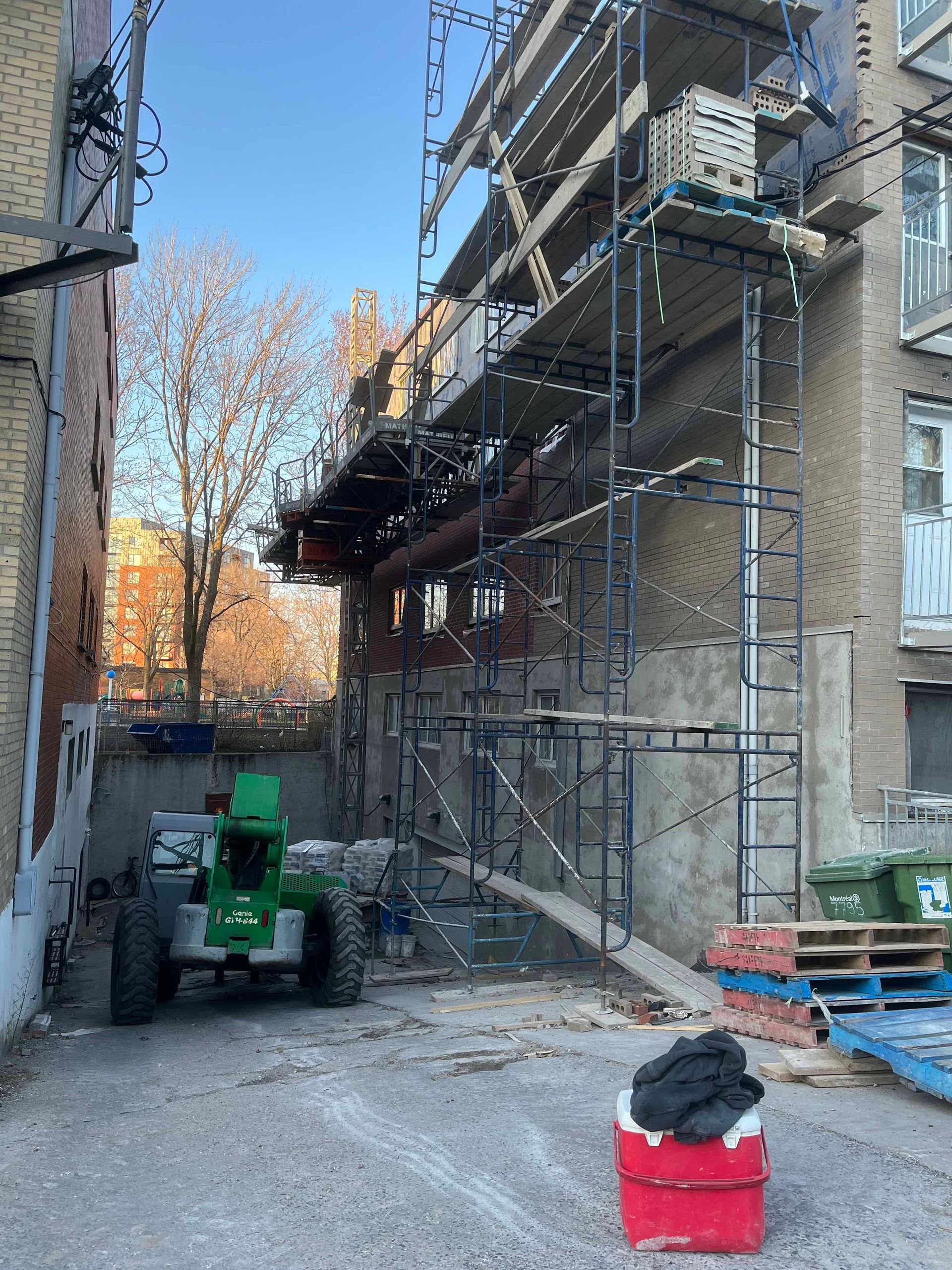 Une glacière rouge est posée devant un bâtiment en construction.