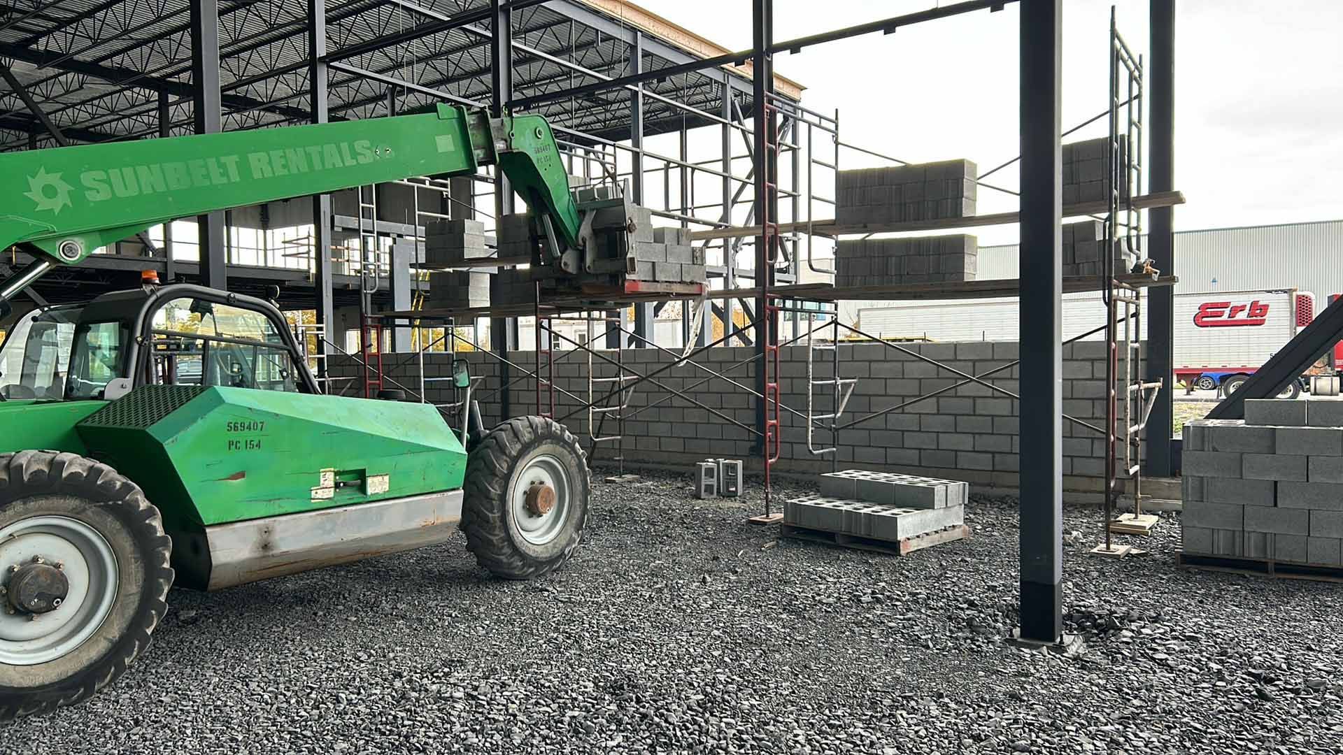 Un chariot élévateur vert est garé devant un bâtiment en construction.
