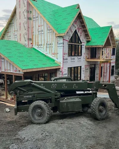 Un tracteur vert est garé devant une maison en construction.