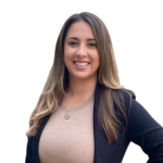 Smiling woman with long hair wearing a black blazer over a beige top against a white background