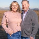 Smiling couple standing outdoors, woman in pink top and man in gray sweater with sunset background