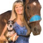 Woman holding a small dog beside a horse with a blue halter, smiling against a white background