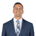 Smiling man in a navy suit, white shirt, and blue patterned tie on a white background