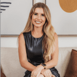 Smiling woman in a black dress sitting indoors against a light wall