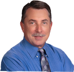 Head-and-shoulders portrait of a smiling man in a blue shirt and patterned tie on a white background