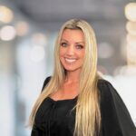 Smiling blonde woman in a black top against a blurred indoor background