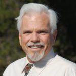 Portrait of a smiling man with white hair and beard wearing a white shirt outdoors