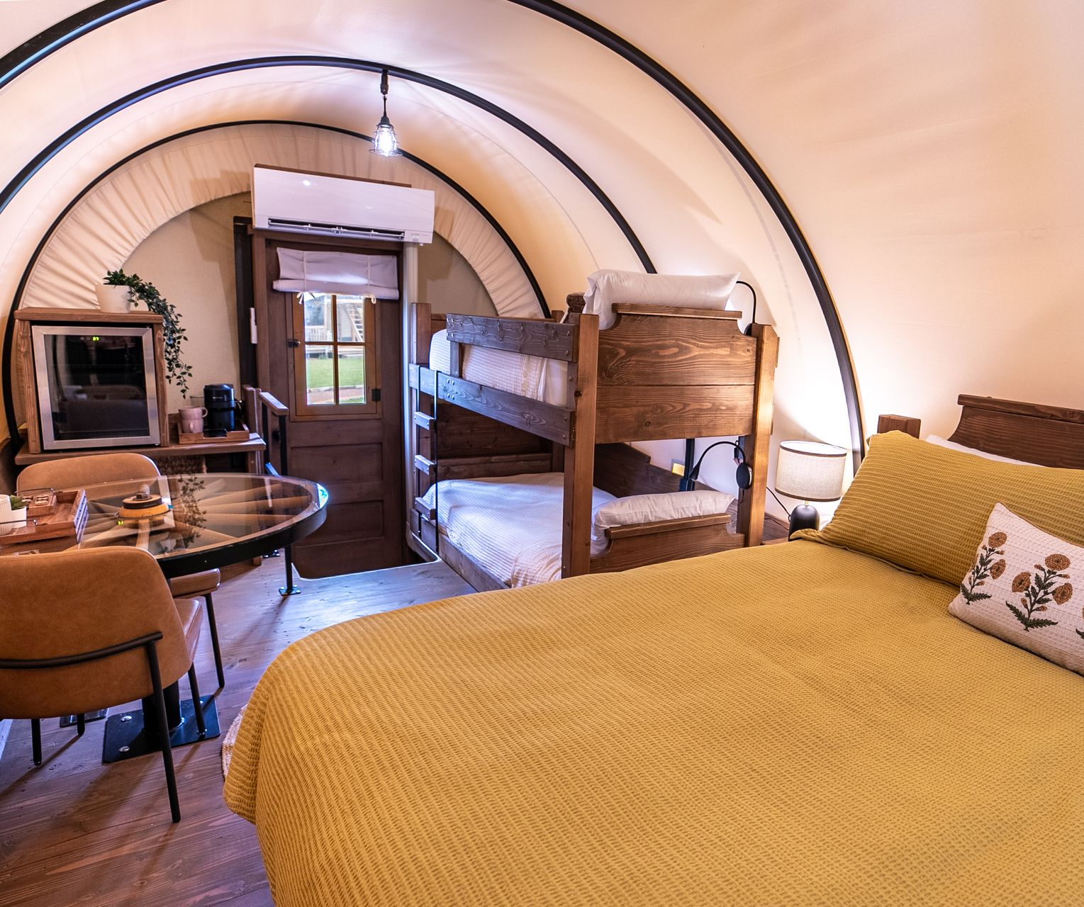 Interior of a Conestoga wagon glamping unit at Clay Cosmos with yellow sunny sheets on the king bed and two twin bunk beds.