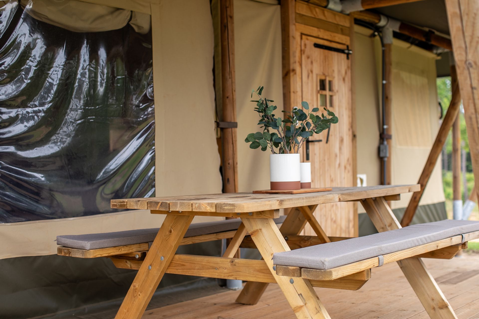 Exterior photo of a canvas cabin at Clay Cosmos glamping resort in Lumpkin georgia with a picnic table and cushioned seats.