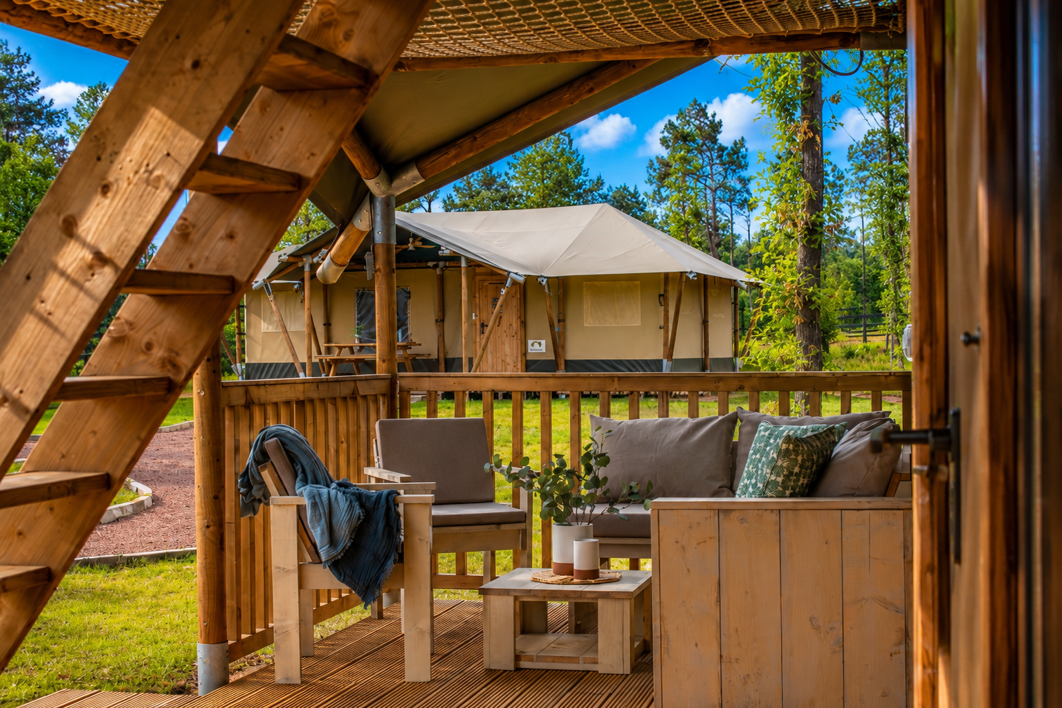 Exterior of front porch at a Canvas Cabin at Clay Cosmos glamping resort, with cushioned outdoor seating and sunny blue skies