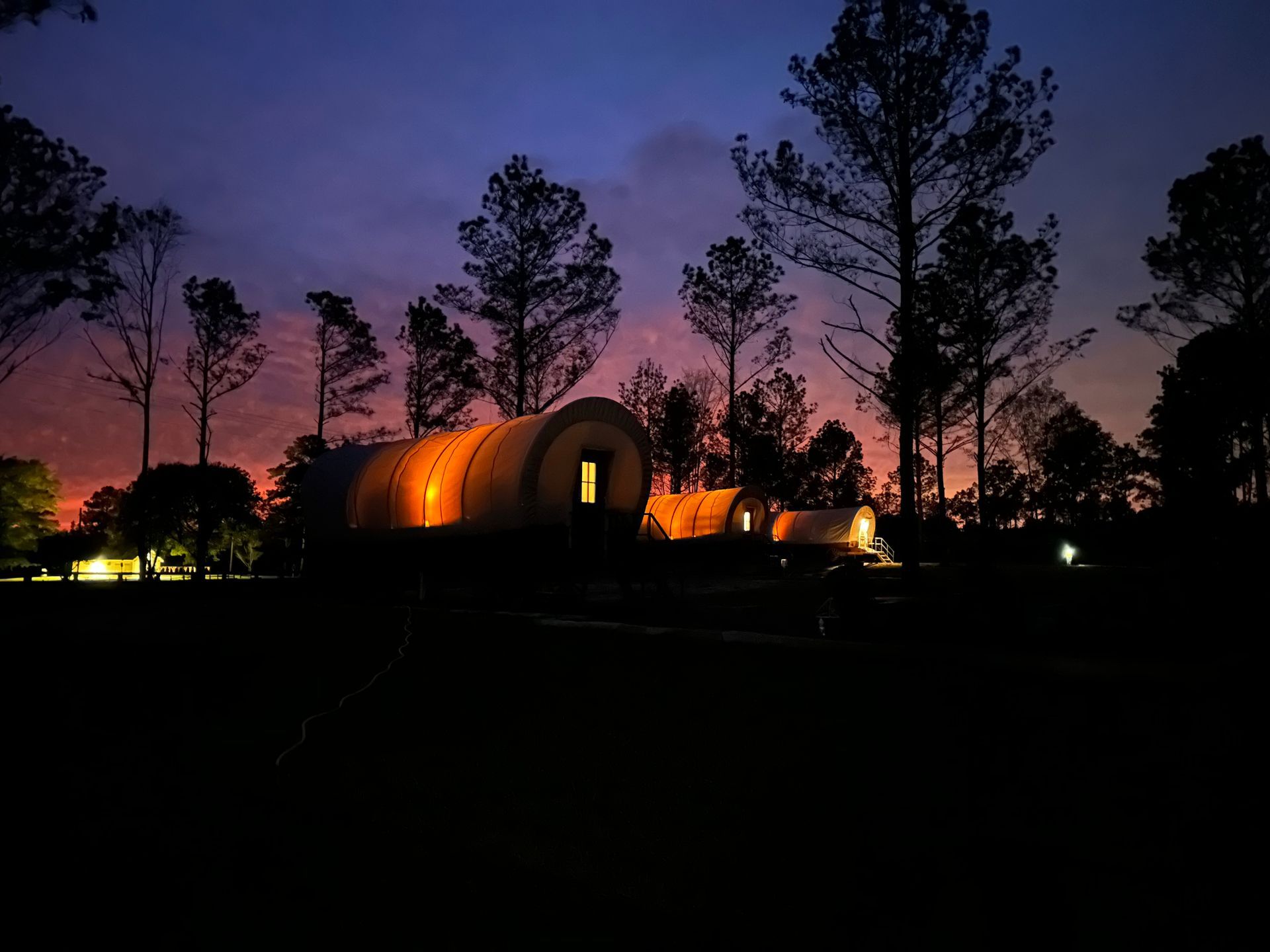 Sunset over Providence Canyon with glowing interiors of Conestoga Wagons at night time at Clay Cosmos in Lumpkin, Georgia