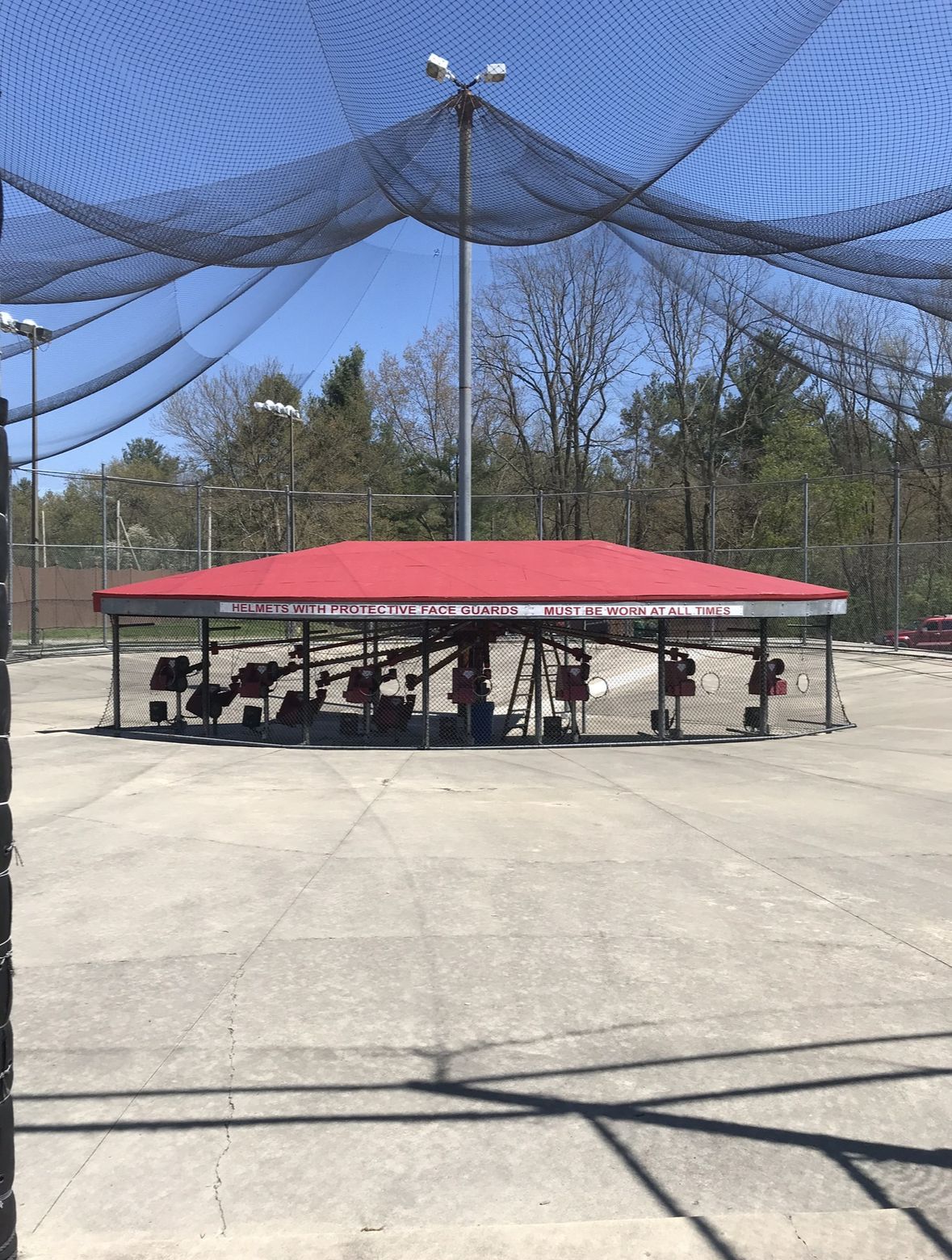 Driving range with red-roofed structure, surrounded by netting, under a blue sky.