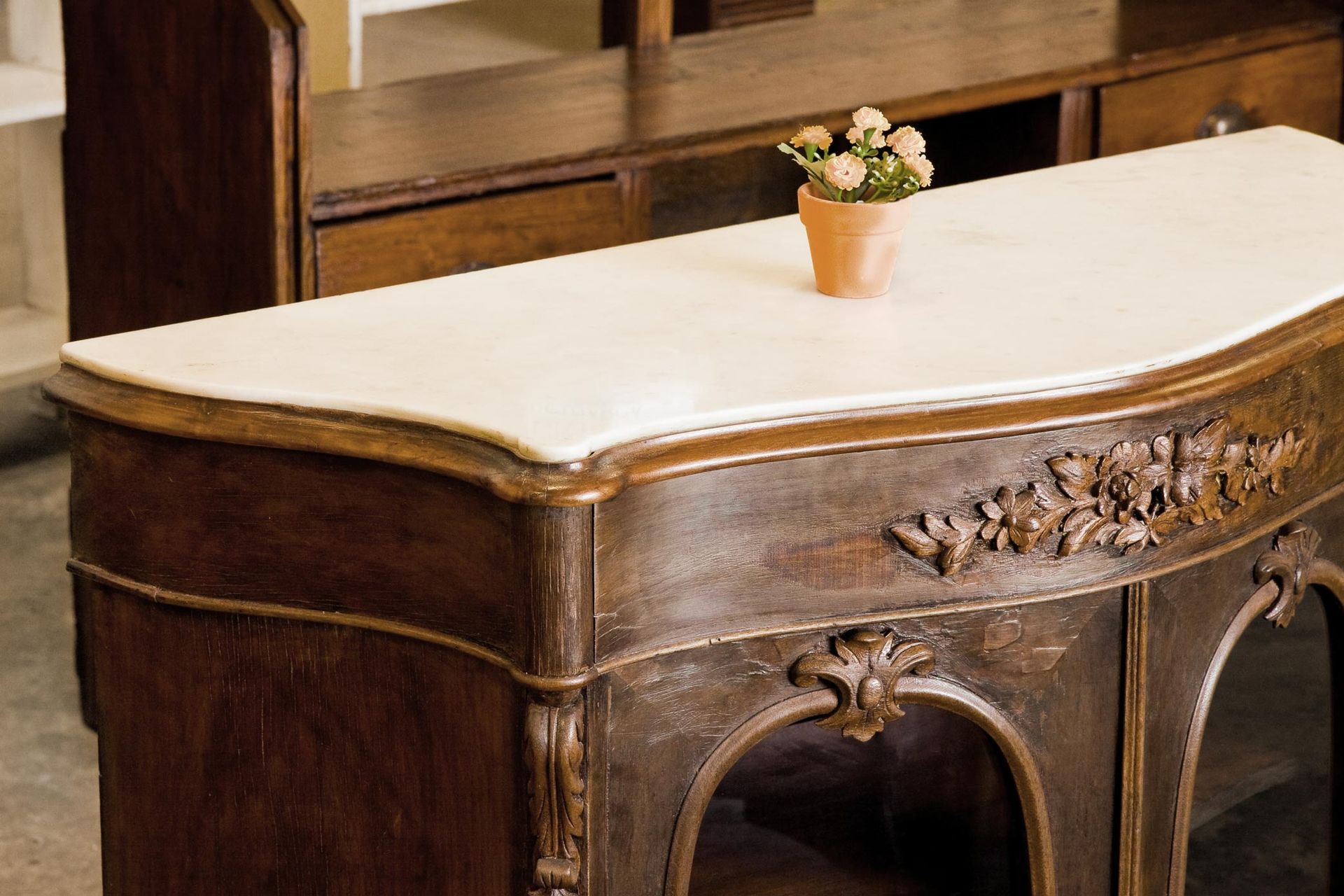 Antique wooden sideboard with marble top and floral carvings, a small potted plant on top.