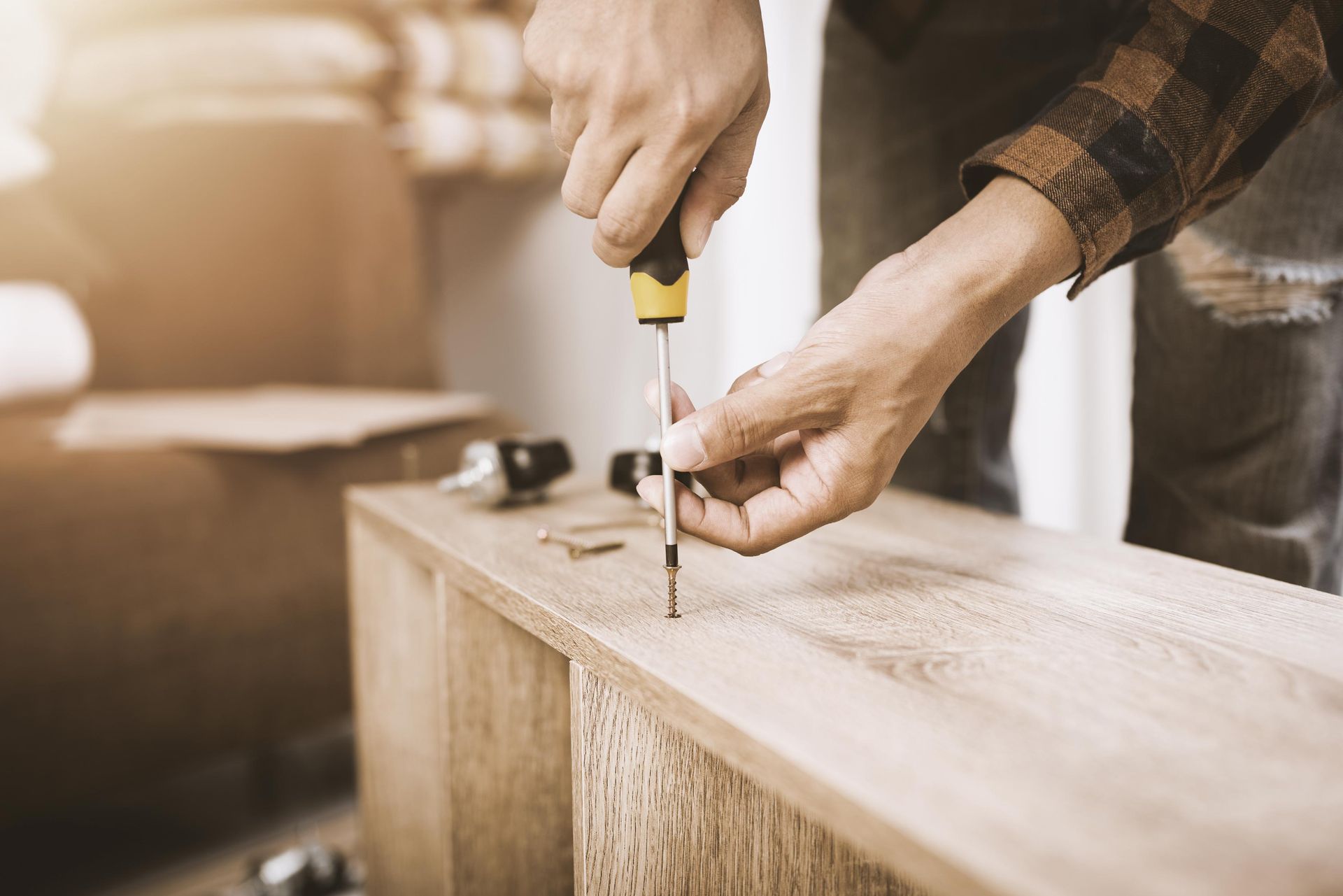 Person using a screwdriver to assemble a wooden furniture piece.