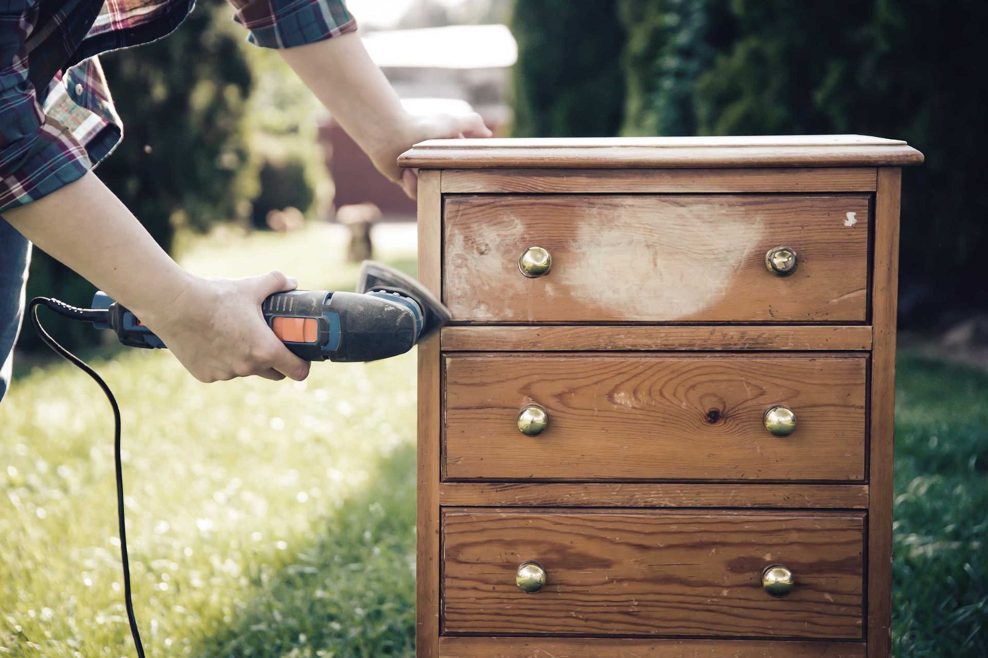 Person sanding a wooden dresser outdoors.