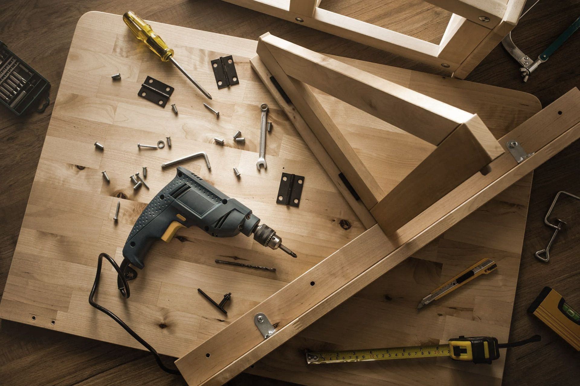 Tools and wood pieces on workbench; a drill, screws, and hardware are in use.