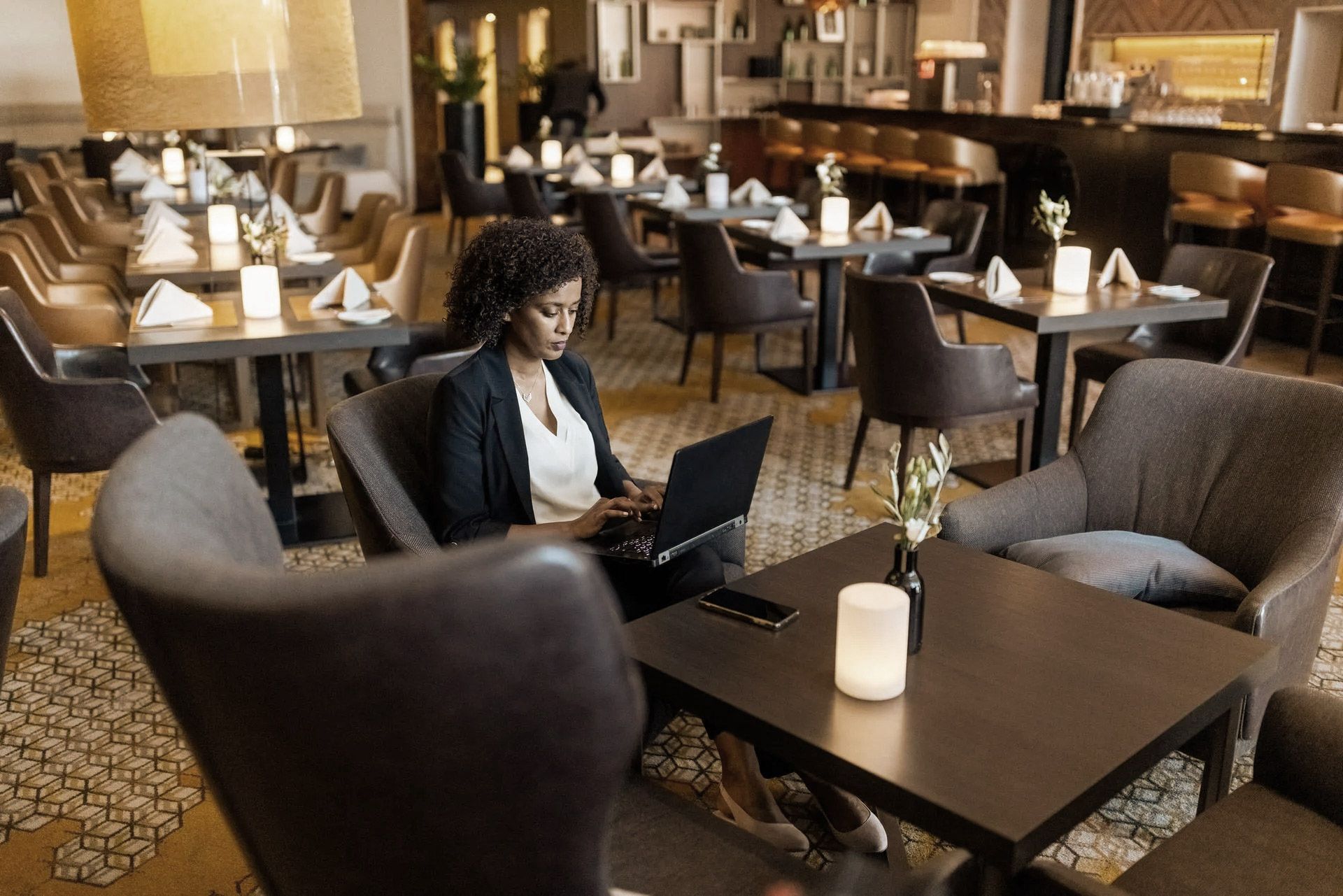 Woman using laptop at a table in a restaurant; other tables and chairs visible.