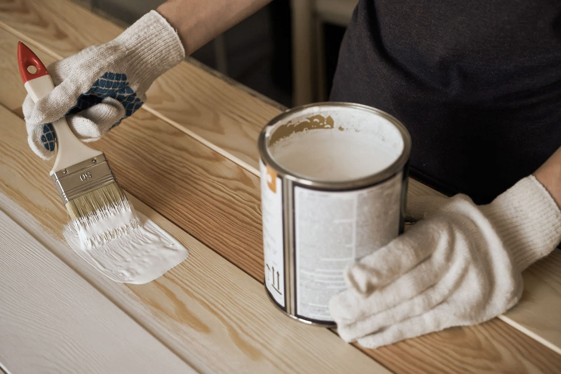 Person wearing gloves painting wood planks with white paint.