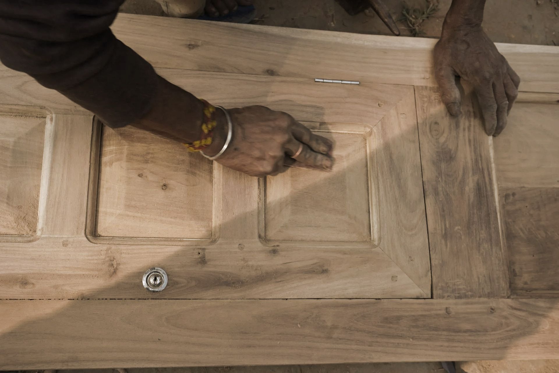 Person's hands smoothing wood door. Door has carved panels, metal hardware.