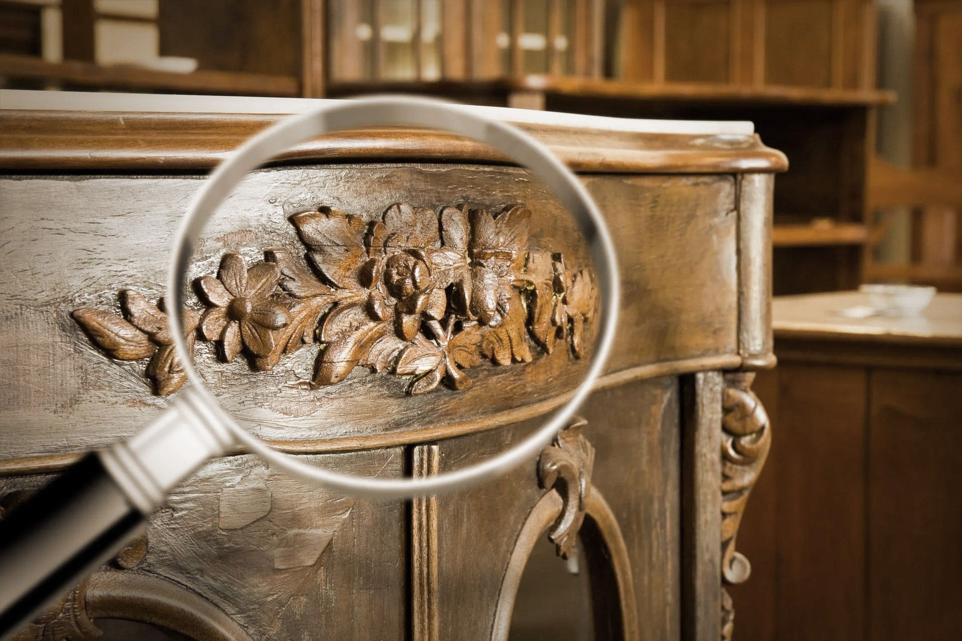 Magnifying glass focusing on a detailed floral carving on antique wooden furniture.
