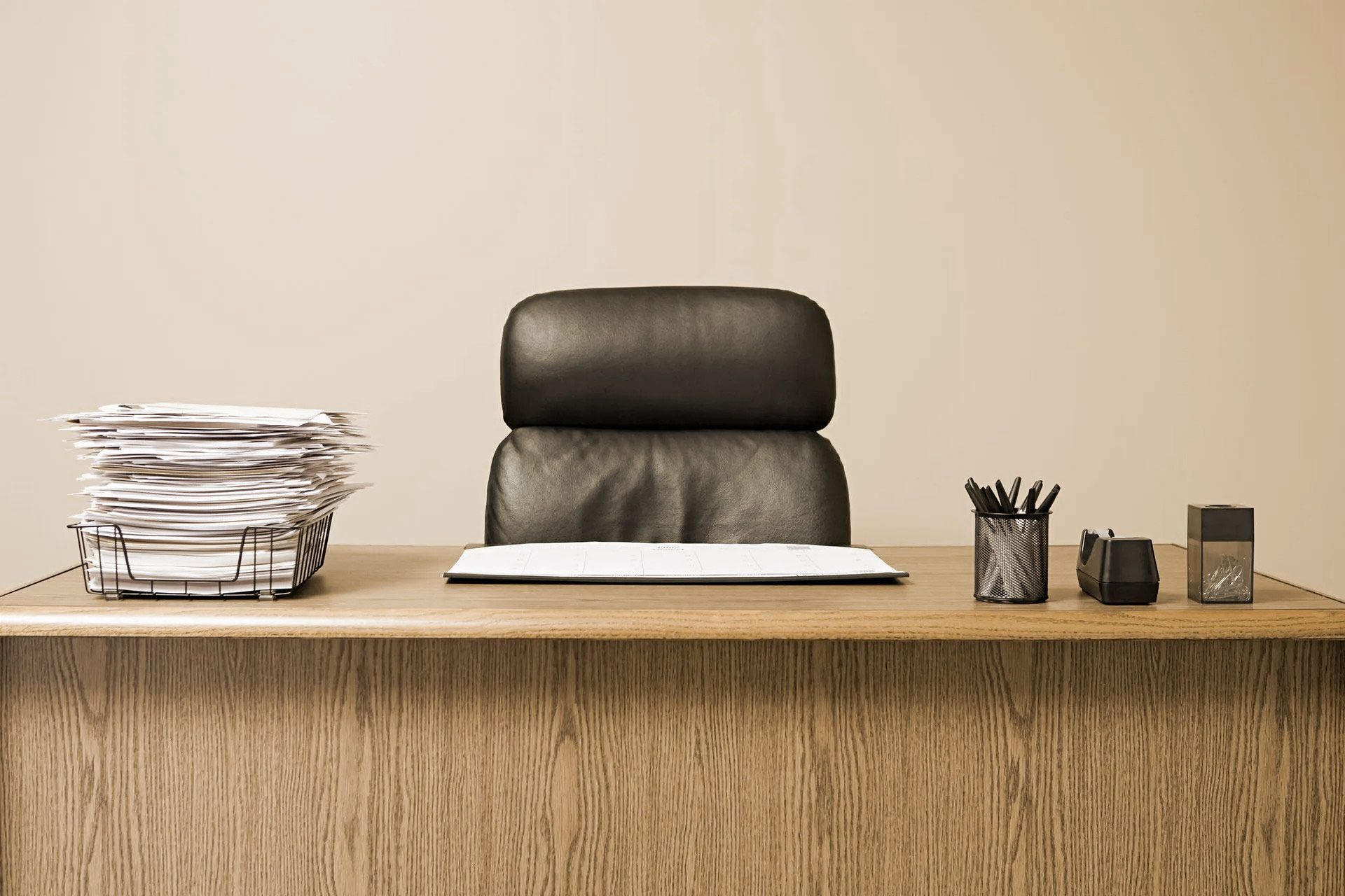 Wooden desk with leather chair, papers, and office supplies.
