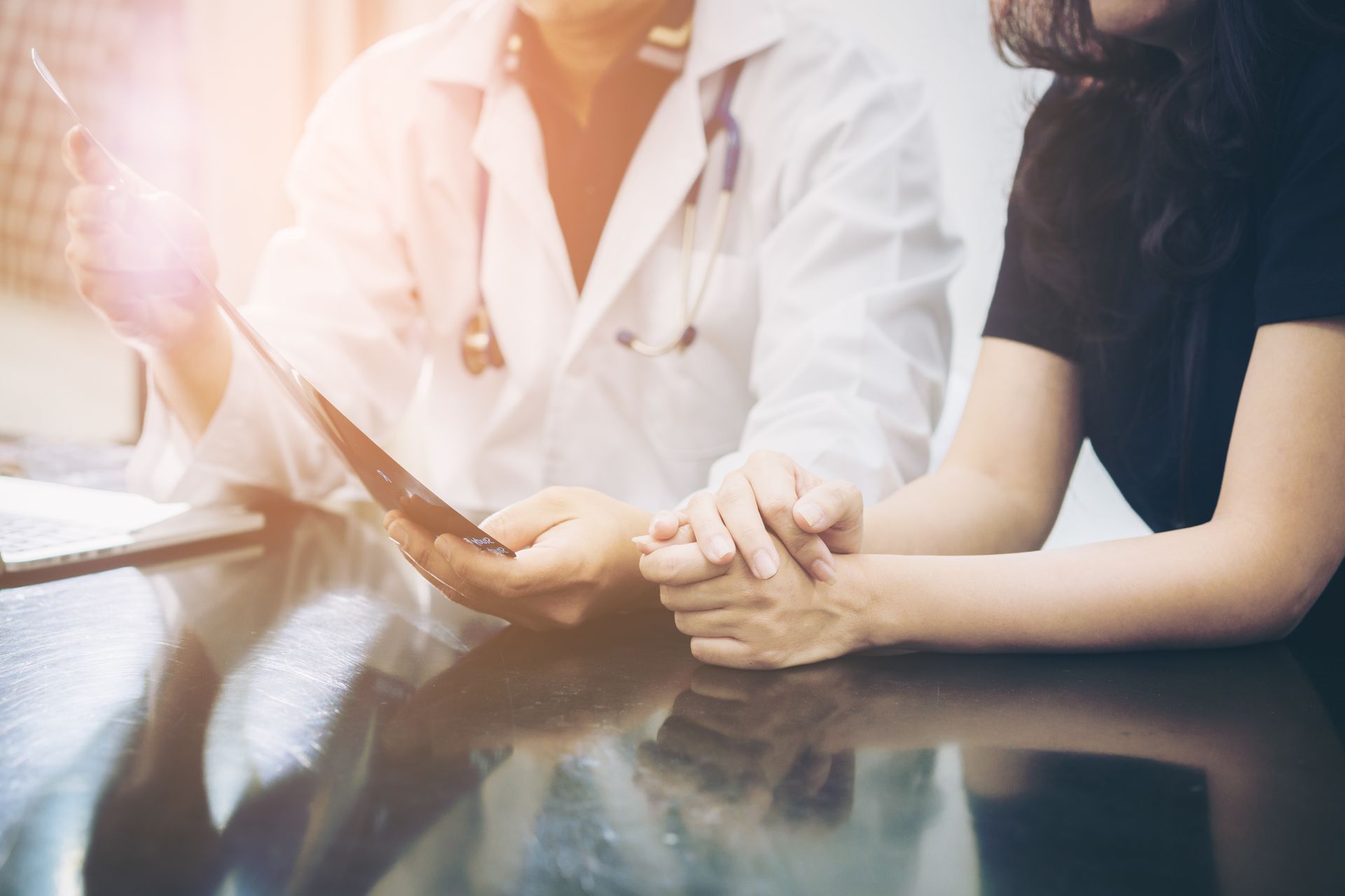 Un médico sostiene la mano de un paciente mientras mira un portapapeles.