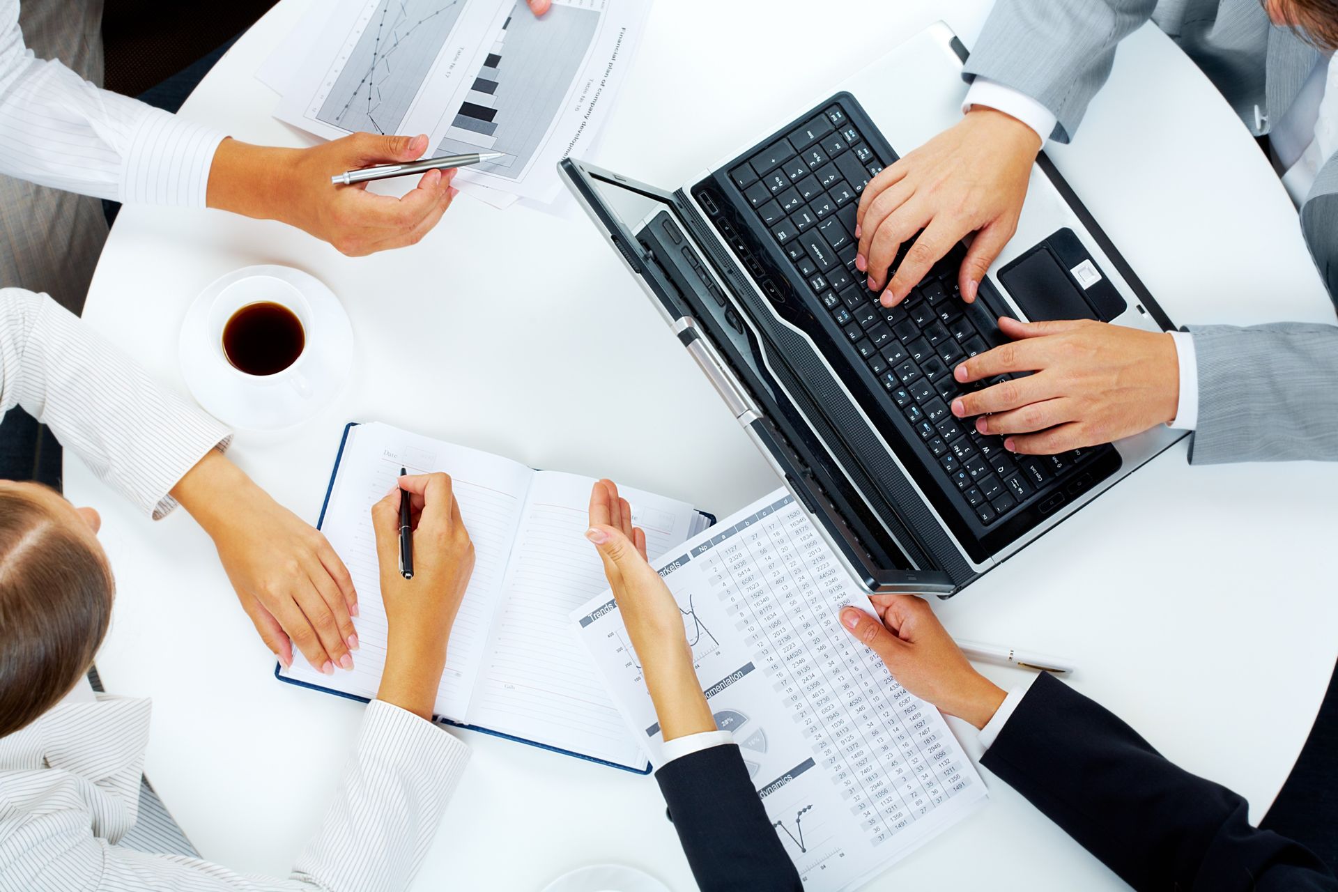 Un gruppo di persone è seduto attorno a un tavolo con computer portatili e documenti.