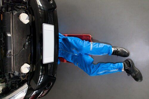 Mechanic in Blue Jumpsuit Working Under a Black Car — Peter Mac's Mechanical in Morisset, NSW