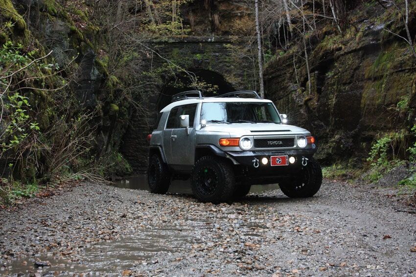 Silver Toyota FJ Cruiser driving through a dark tunnel on a gravel road.