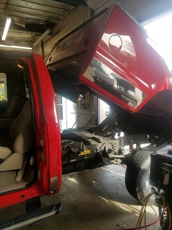 A red truck with the hood up is sitting in a garage.
