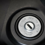 Close-up of a car ignition with settings: lock, ACC, on, and start. Black surround with a silver ignition slot.