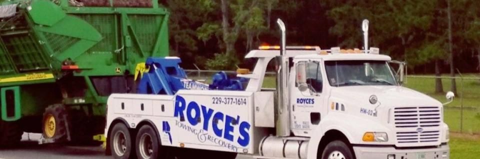 Tow truck, Royce's Towing, towing large green agricultural equipment. White truck, blue tow equipment.