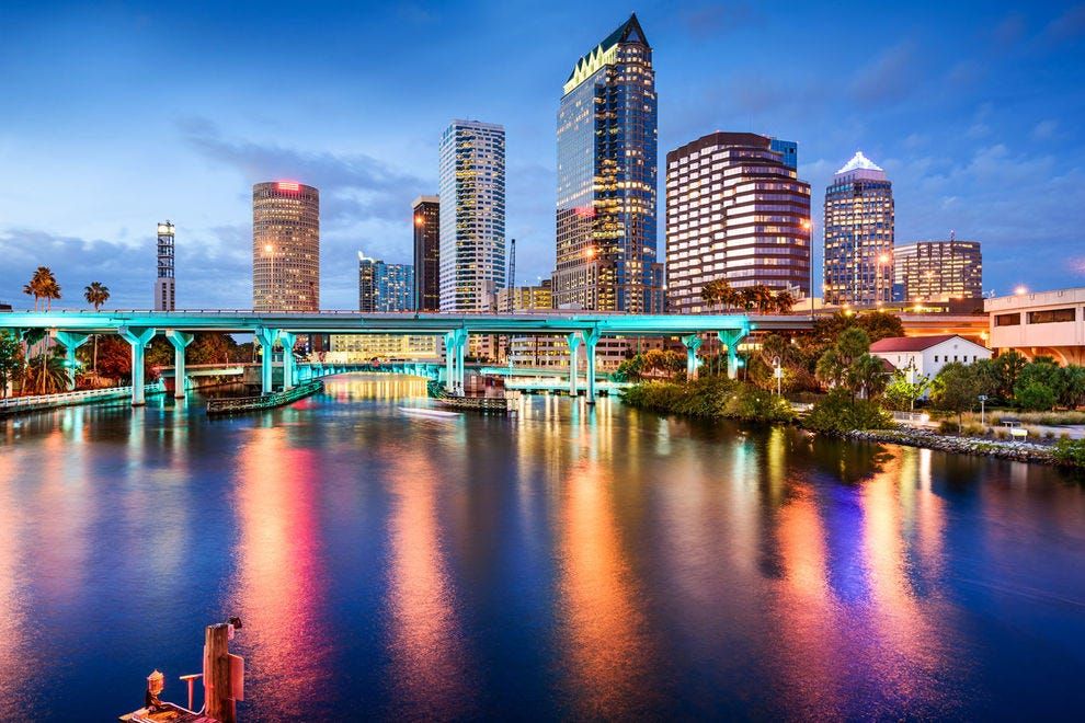 Tampa, Florida skyline at dusk, reflections on water. Illuminated bridge and city buildings.
