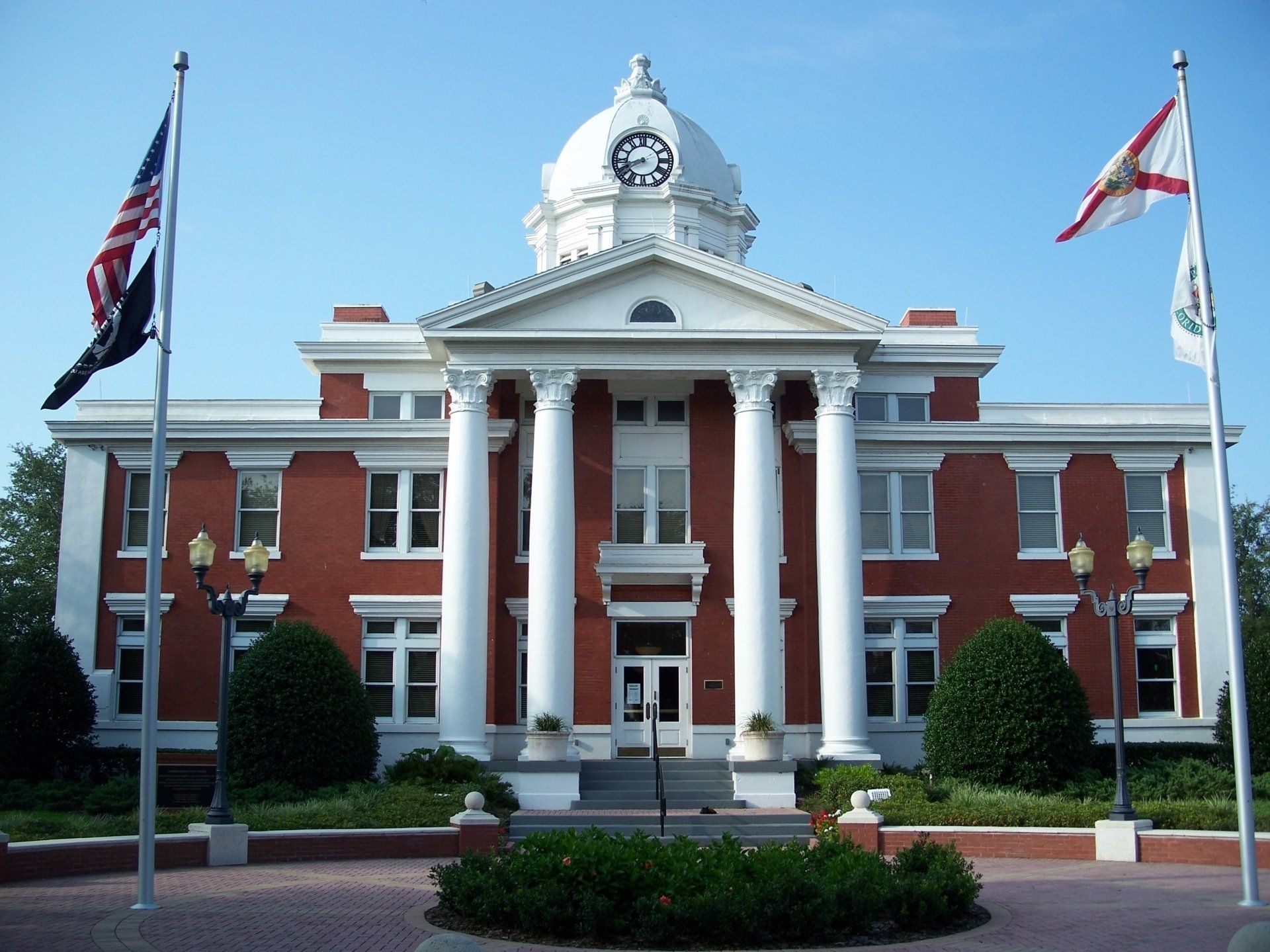 Red brick courthouse with white columns, clock tower, and American and Florida flags.