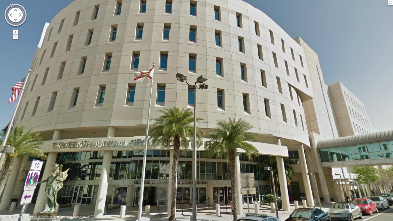 Broward County Courthouse in Fort Lauderdale, Florida. Tall, tan building with glass entrance, palm trees, and flags.