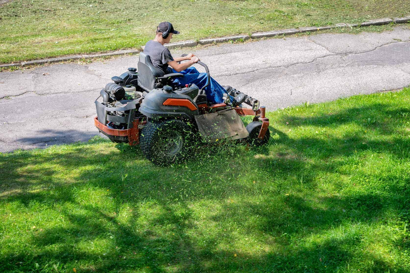 Person riding a red-and-black lawn mower across a grassy slope near a paved path.