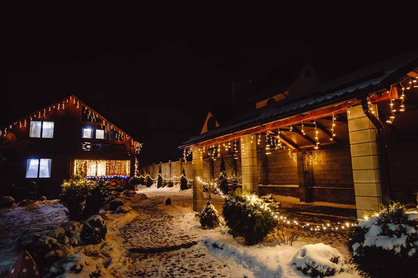 Snowy cabin and lit wooden house at night with warm string lights and glowing windows