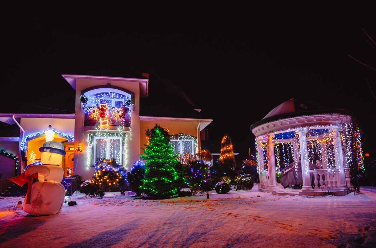 Snowy house decorated with colorful Christmas lights and a lit gazebo at night