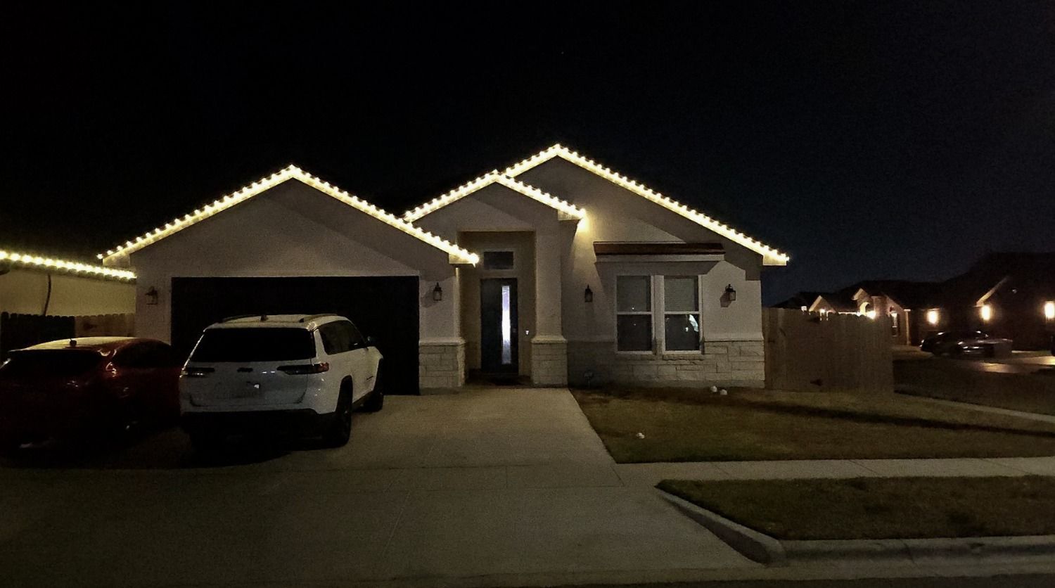 Suburban house at night with roofline lights, a white SUV in the driveway, and a dark garage.