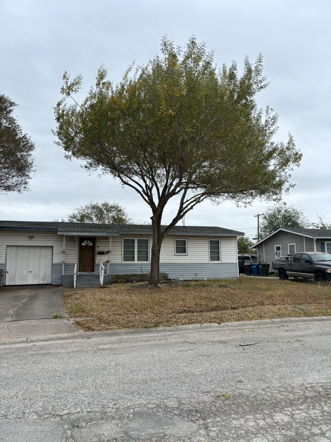 Single-story house with a large tree in front, a driveway on the left, and a parked pickup on the right.