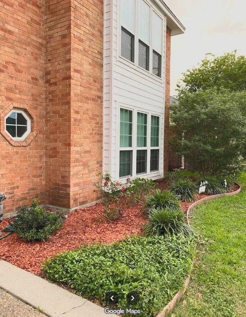 Brick and white townhouse exterior with landscaped mulch beds and green shrubs beside a lawn