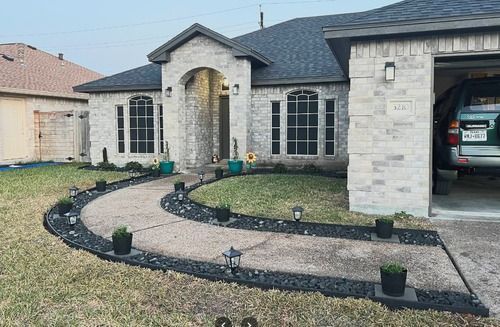 Front view of a stone house with curved gravel walkway, small lights, and a car parked in the garage.