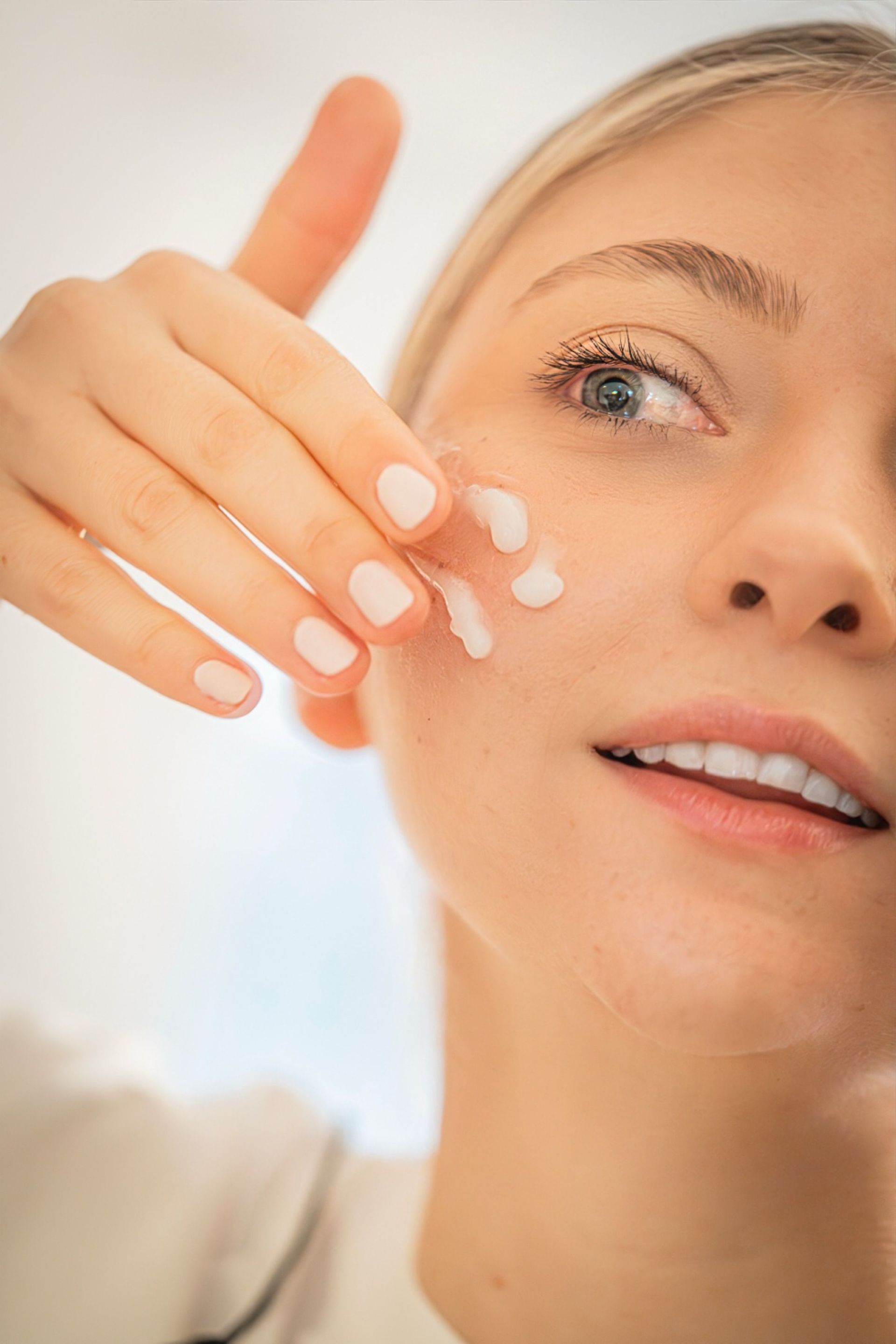 Close-up of a person applying white cream to their cheek and finger, with a bright skincare look