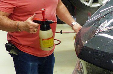 Un homme pulvérise du produit sur une voiture avec un vaporisateur.