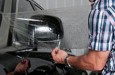 Un homme enveloppe une voiture avec du film plastique.