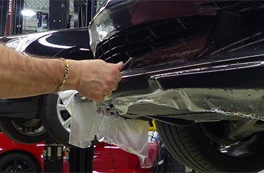 Un homme enveloppe le dessous d'une voiture avec du plastique.