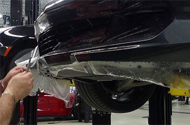 Une personne recouvre le dessous d'une voiture avec du plastique.