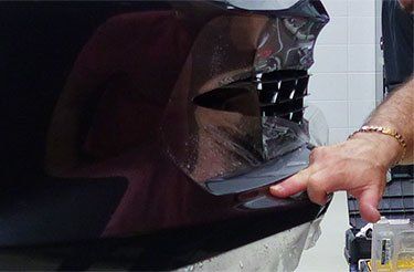 Un homme enveloppe un pare-chocs de voiture avec du film plastique.